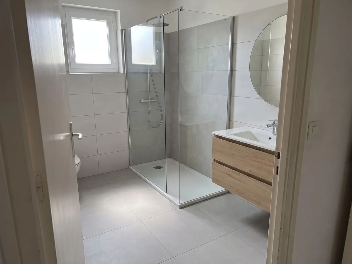 Après : la même salle de bain avec une douche à l’italienne, carrelage blanc et meuble en bois