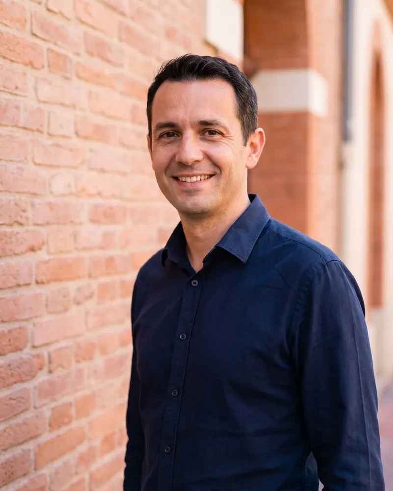 Julien, la quarantaine, chemise bleu nuit, souriant devant un mur de brique
