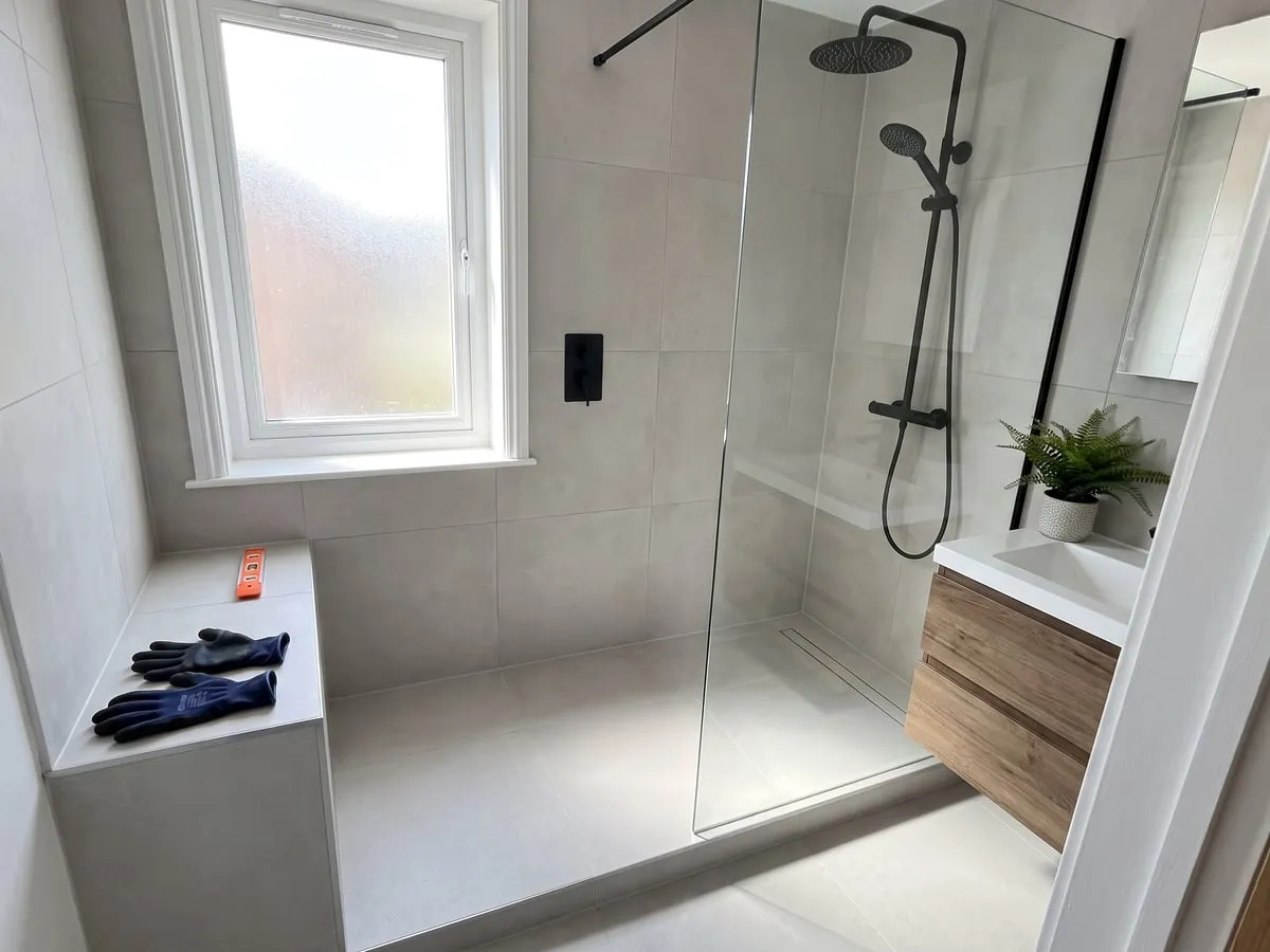 Douche à l’italienne terminée, paroi vitrée, carrelage clair et robinetterie noire