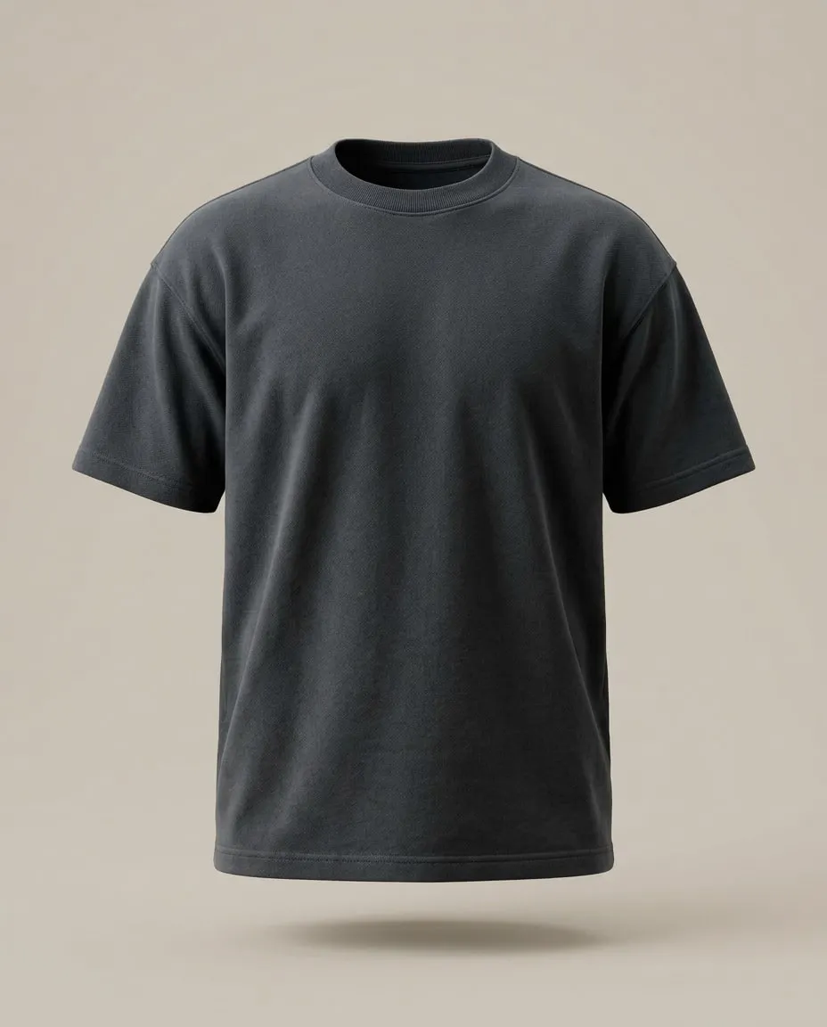 Le T-shirt Épais gris charbon, de face, comme porté, sur un fond de pierre claire : épaules tombantes et col côtelé épais