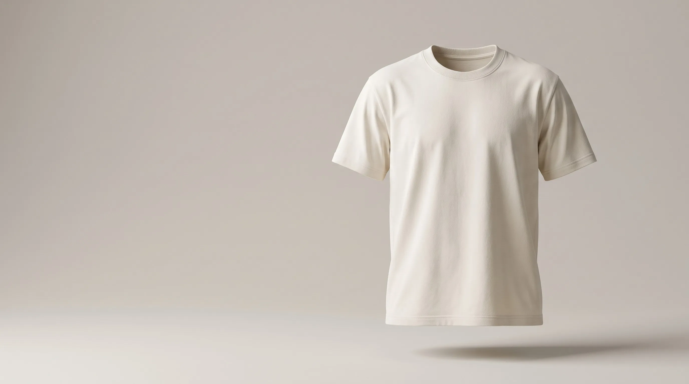 Un t-shirt écru en coton épais, comme porté par un corps invisible, en suspension dans un studio gris pierre